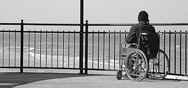 Young man in a wheelchair looks over railings towrds the sea